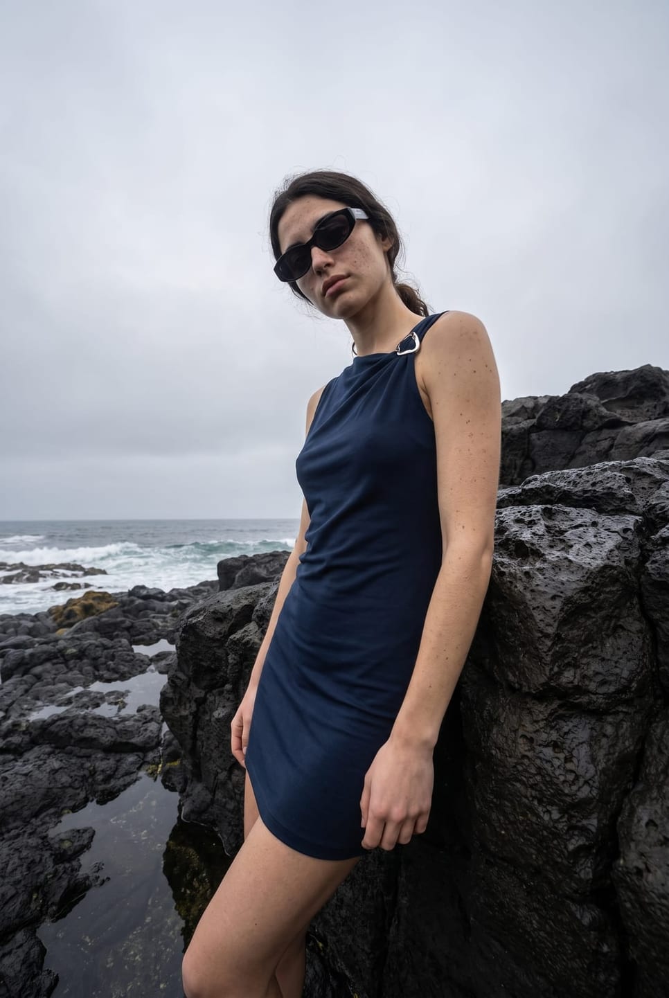 The same synthetic talent leaning against black volcanic rock above the sea — not a real person