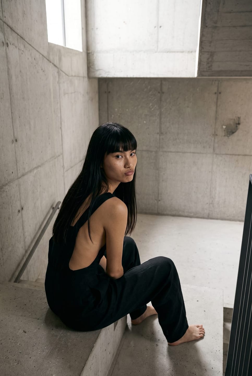 Synthetic talent in a black jumpsuit seen from behind, looking back over the shoulder — not a real person