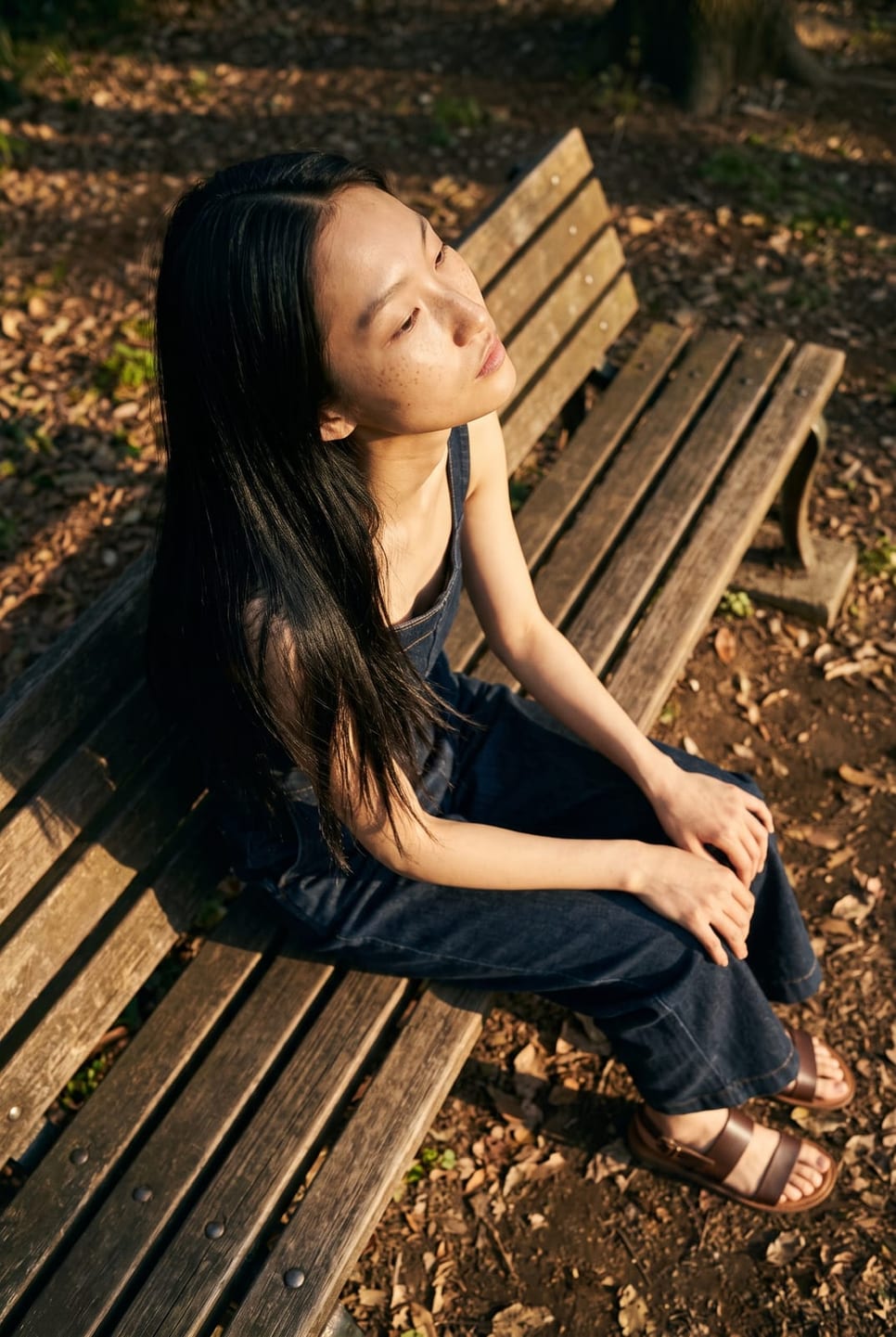 Synthetic talent on a woodland bench, turned away, hair across the shoulder — not a real person