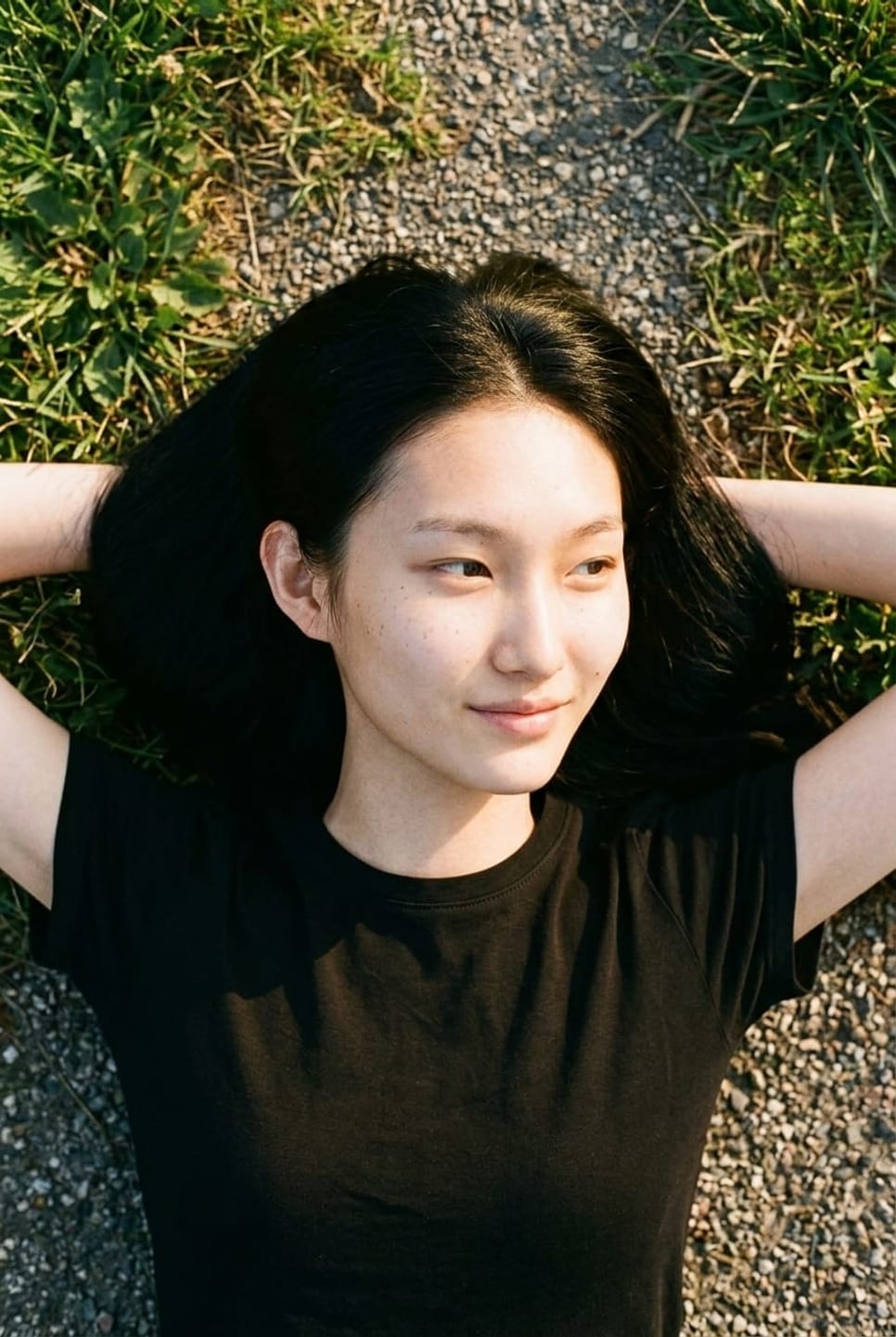 Synthetic talent lying on grass, shot from overhead, arms behind the head — not a real person